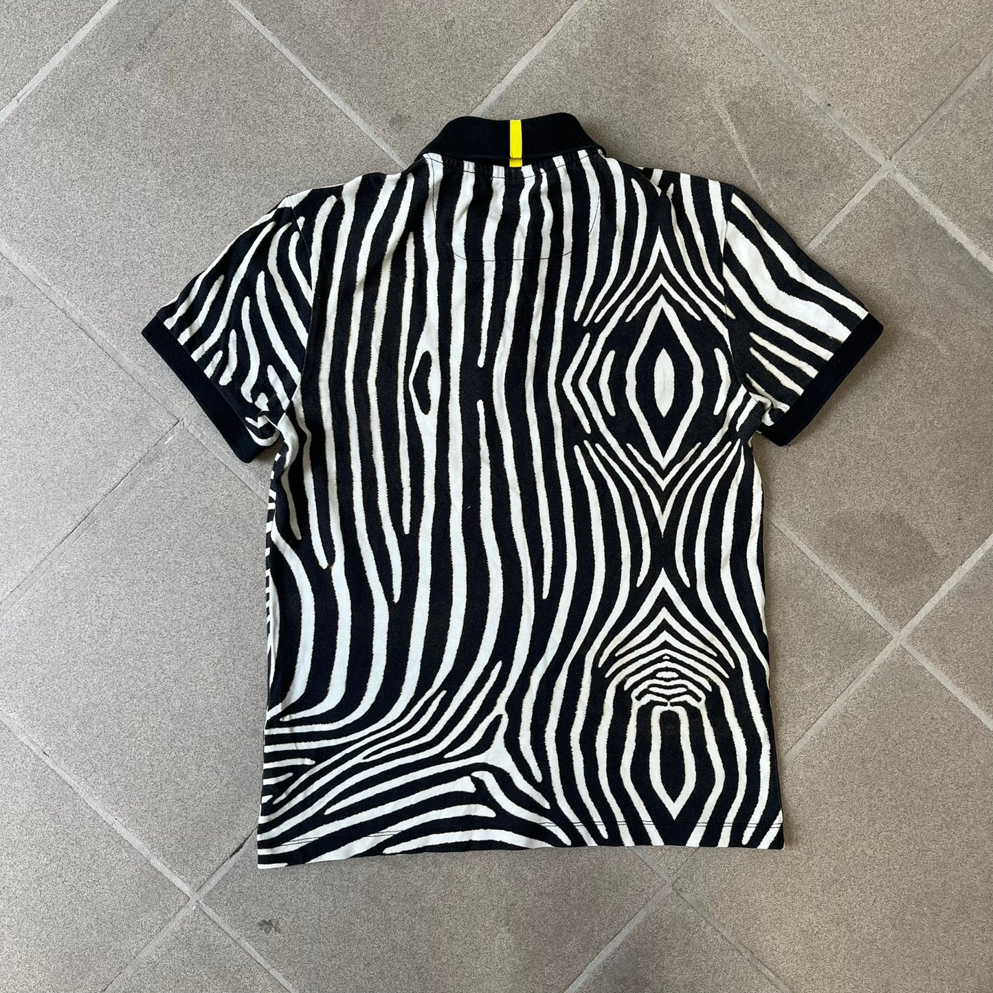 Lacoste x National Geographic AW20 Zebra Polo features an all-over white and black zebra print pattern across the fabric. The polo has black collar and sleeve hems, with a chest patch featuring the Lacoste crocodile logo in matching pattern colors.