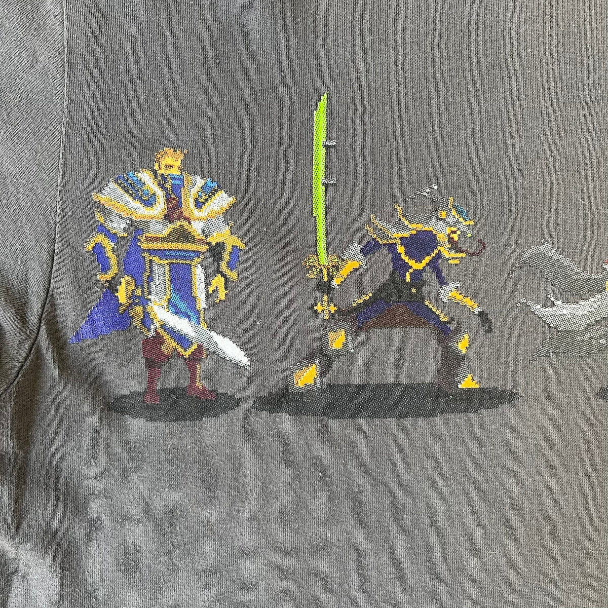 League of Legends 2013 Pixel Team Gray Tee is a gray T-shirt featuring a full five-champion team (Garen, Master Yi, Ahri, Ashe, and Kayle) rendered in pixel art style on the front. The upper back shows League main Logo. Licensed 2013 neck tag with the old Riot Games logo.