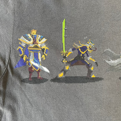 League of Legends 2013 Pixel Team Gray Tee is a gray T-shirt featuring a full five-champion team (Garen, Master Yi, Ahri, Ashe, and Kayle) rendered in pixel art style on the front. The upper back shows League main Logo. Licensed 2013 neck tag with the old Riot Games logo.