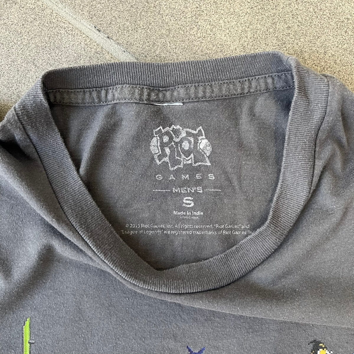 League of Legends 2013 Pixel Team Gray Tee is a gray T-shirt featuring a full five-champion team (Garen, Master Yi, Ahri, Ashe, and Kayle) rendered in pixel art style on the front. The upper back shows League main Logo. Licensed 2013 neck tag with the old Riot Games logo.