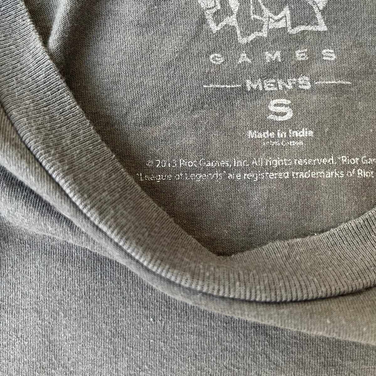 League of Legends 2013 Pixel Team Gray Tee is a gray T-shirt featuring a full five-champion team (Garen, Master Yi, Ahri, Ashe, and Kayle) rendered in pixel art style on the front. The upper back shows League main Logo. Licensed 2013 neck tag with the old Riot Games logo.