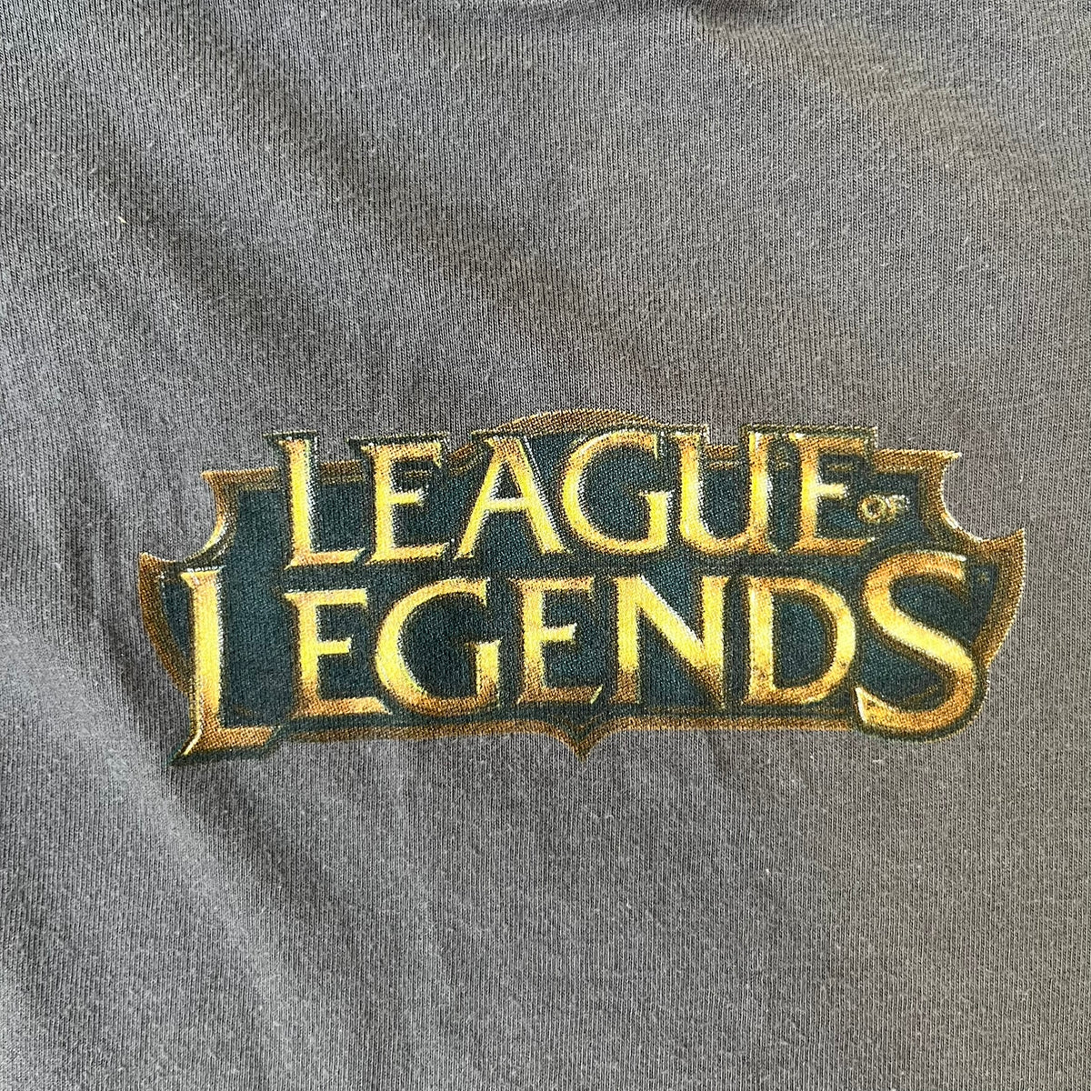 League of Legends 2013 Pixel Team Gray Tee is a gray T-shirt featuring a full five-champion team (Garen, Master Yi, Ahri, Ashe, and Kayle) rendered in pixel art style on the front. The upper back shows League main Logo. Licensed 2013 neck tag with the old Riot Games logo.