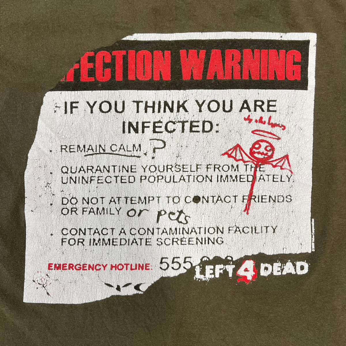 Left 4 Dead 2009 Infection Warning Tee features a khaki T-shirt with a distressed poster-style graphic on the front. The graphic has red “Infection Warning” text, instructions on what to do when infected, an emergency hotline number, and scribbled details. A Left 4 Dead logo and small 2009 Valve licensing appear underneath. The upper back features a Left 4 Dead logo with a blood splatter graphic.