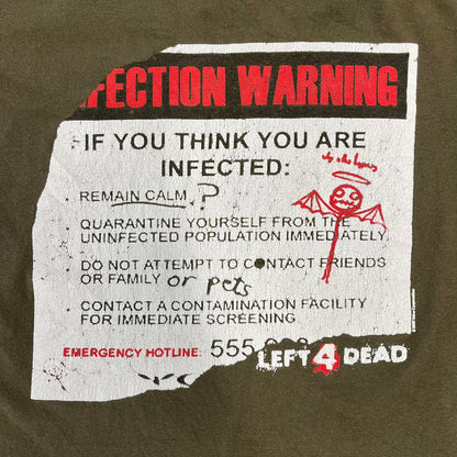 Left 4 Dead 2009 Infection Warning Tee features a khaki T-shirt with a distressed poster-style graphic on the front. The graphic has red “Infection Warning” text, instructions on what to do when infected, an emergency hotline number, and scribbled details. A Left 4 Dead logo and small 2009 Valve licensing appear underneath. The upper back features a Left 4 Dead logo with a blood splatter graphic.