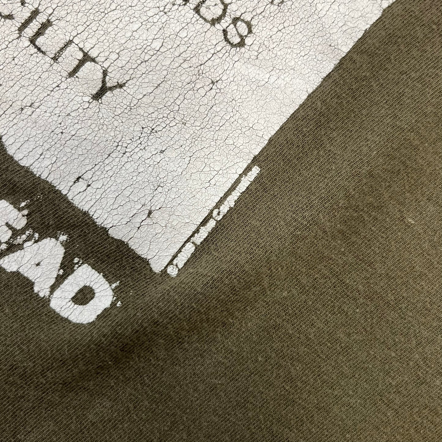 Left 4 Dead 2009 Infection Warning Tee features a khaki T-shirt with a distressed poster-style graphic on the front. The graphic has red “Infection Warning” text, instructions on what to do when infected, an emergency hotline number, and scribbled details. A Left 4 Dead logo and small 2009 Valve licensing appear underneath. The upper back features a Left 4 Dead logo with a blood splatter graphic.