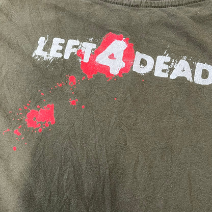 Left 4 Dead 2009 Infection Warning Tee features a khaki T-shirt with a distressed poster-style graphic on the front. The graphic has red “Infection Warning” text, instructions on what to do when infected, an emergency hotline number, and scribbled details. A Left 4 Dead logo and small 2009 Valve licensing appear underneath. The upper back features a Left 4 Dead logo with a blood splatter graphic.