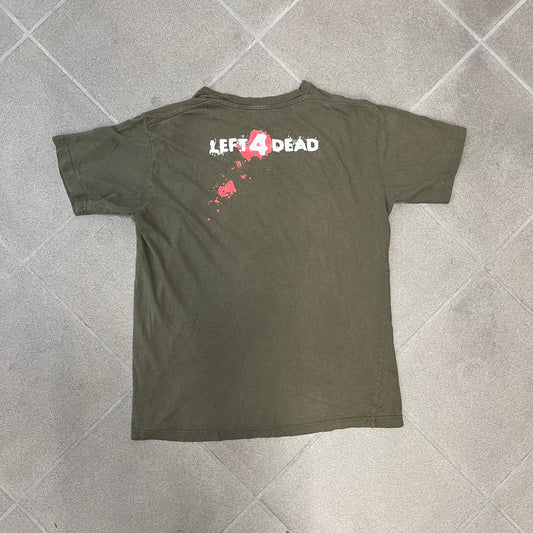 Left 4 Dead 2009 Infection Warning Tee features a khaki T-shirt with a distressed poster-style graphic on the front. The graphic has red “Infection Warning” text, instructions on what to do when infected, an emergency hotline number, and scribbled details. A Left 4 Dead logo and small 2009 Valve licensing appear underneath. The upper back features a Left 4 Dead logo with a blood splatter graphic.