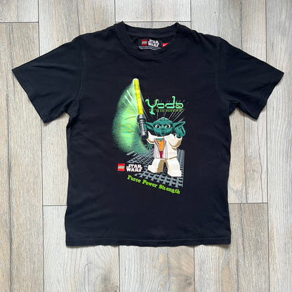 LEGO Yoda “Jedi Master” 2009 Tee is a black short-sleeve t-shirt featuring a front graphic of Yoda swinging a green lightsaber. Above the graphic is “Yoda Jedi Master” text in green, with “Force Power Strength” printed underneath. The tee includes a LEGO Star Wars 2009 neck tag.