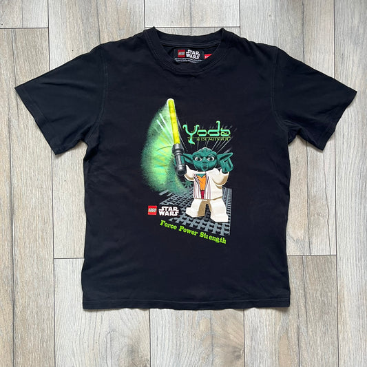 LEGO Yoda “Jedi Master” 2009 Tee is a black short-sleeve t-shirt featuring a front graphic of Yoda swinging a green lightsaber. Above the graphic is “Yoda Jedi Master” text in green, with “Force Power Strength” printed underneath. The tee includes a LEGO Star Wars 2009 neck tag.