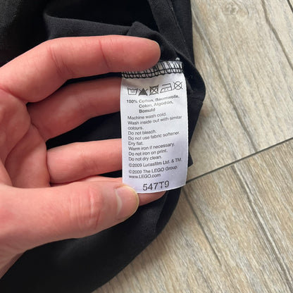 LEGO Yoda “Jedi Master” 2009 Tee is a black short-sleeve t-shirt featuring a front graphic of Yoda swinging a green lightsaber. Above the graphic is “Yoda Jedi Master” text in green, with “Force Power Strength” printed underneath. The tee includes a LEGO Star Wars 2009 neck tag.