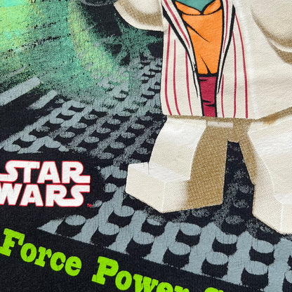 LEGO Yoda “Jedi Master” 2009 Tee is a black short-sleeve t-shirt featuring a front graphic of Yoda swinging a green lightsaber. Above the graphic is “Yoda Jedi Master” text in green, with “Force Power Strength” printed underneath. The tee includes a LEGO Star Wars 2009 neck tag.