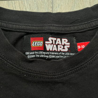 LEGO Yoda “Jedi Master” 2009 Tee is a black short-sleeve t-shirt featuring a front graphic of Yoda swinging a green lightsaber. Above the graphic is “Yoda Jedi Master” text in green, with “Force Power Strength” printed underneath. The tee includes a LEGO Star Wars 2009 neck tag.