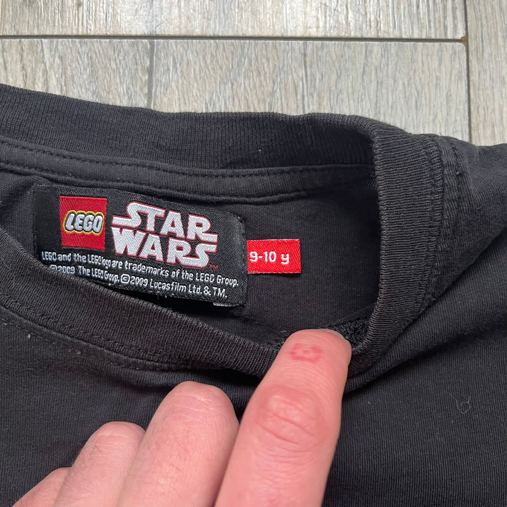 LEGO Yoda “Jedi Master” 2009 Tee is a black short-sleeve t-shirt featuring a front graphic of Yoda swinging a green lightsaber. Above the graphic is “Yoda Jedi Master” text in green, with “Force Power Strength” printed underneath. The tee includes a LEGO Star Wars 2009 neck tag.