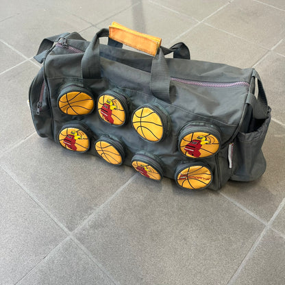 Lego Basketball 2003 Multi Pocket Gray Bag is a gray gym bag with orange side panels and an orange strap handle, featuring a Lego Sports tag. The front is designed to resemble a Lego 8x2 brick, with 8 zippable circular pockets featuring basketball orange graphics or basketball player designs.