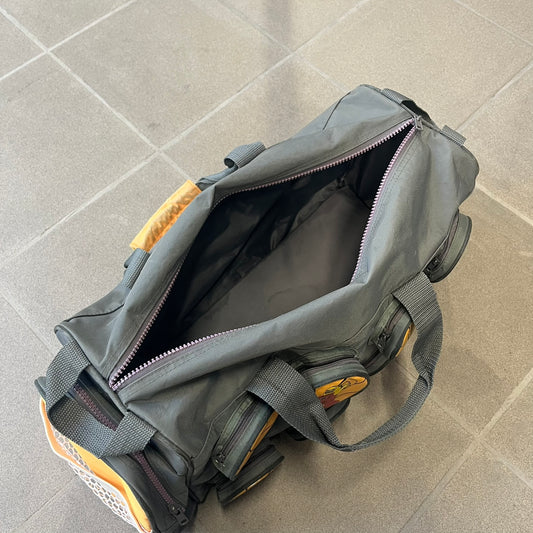 Lego Basketball 2003 Multi Pocket Gray Bag is a gray gym bag with orange side panels and an orange strap handle, featuring a Lego Sports tag. The front is designed to resemble a Lego 8x2 brick, with 8 zippable circular pockets featuring basketball orange graphics or basketball player designs.