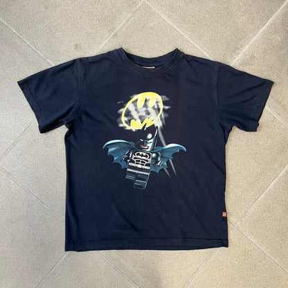 Lego Batman 2006 TS39 Promo Tee is a black T-shirt released alongside the first Lego Batman sets in 2006, featuring a Lego Batman graphic on the front and a clouded Bat-Signal on the back. A licensed 2006 Lego Batman patch sits on the upper back, and it has a Lego Collection neck tag and a small Lego tag on the side. This tee has no size tag.