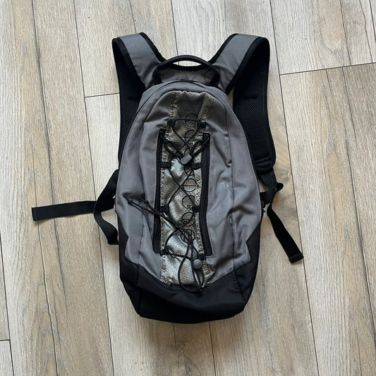 Lego Bionicle 2000s Matoran Alphabet Backpack is a backpack featuring a front design spelling “Bionicle” using the Matoran alphabet. The bag includes two front exterior pockets, a main compartment with three internal pockets, and a top media port for headphones. Additional details include padded and vented back panel, adjustable shoulder straps with chest connector and waist strap, top handle, and elastic cross straps on the front for extra storage.

