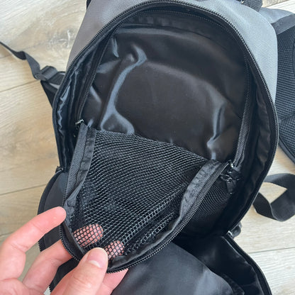 Lego Bionicle 2000s Matoran Alphabet Backpack is a backpack featuring a front design spelling “Bionicle” using the Matoran alphabet. The bag includes two front exterior pockets, a main compartment with three internal pockets, and a top media port for headphones. Additional details include padded and vented back panel, adjustable shoulder straps with chest connector and waist strap, top handle, and elastic cross straps on the front for extra storage.
