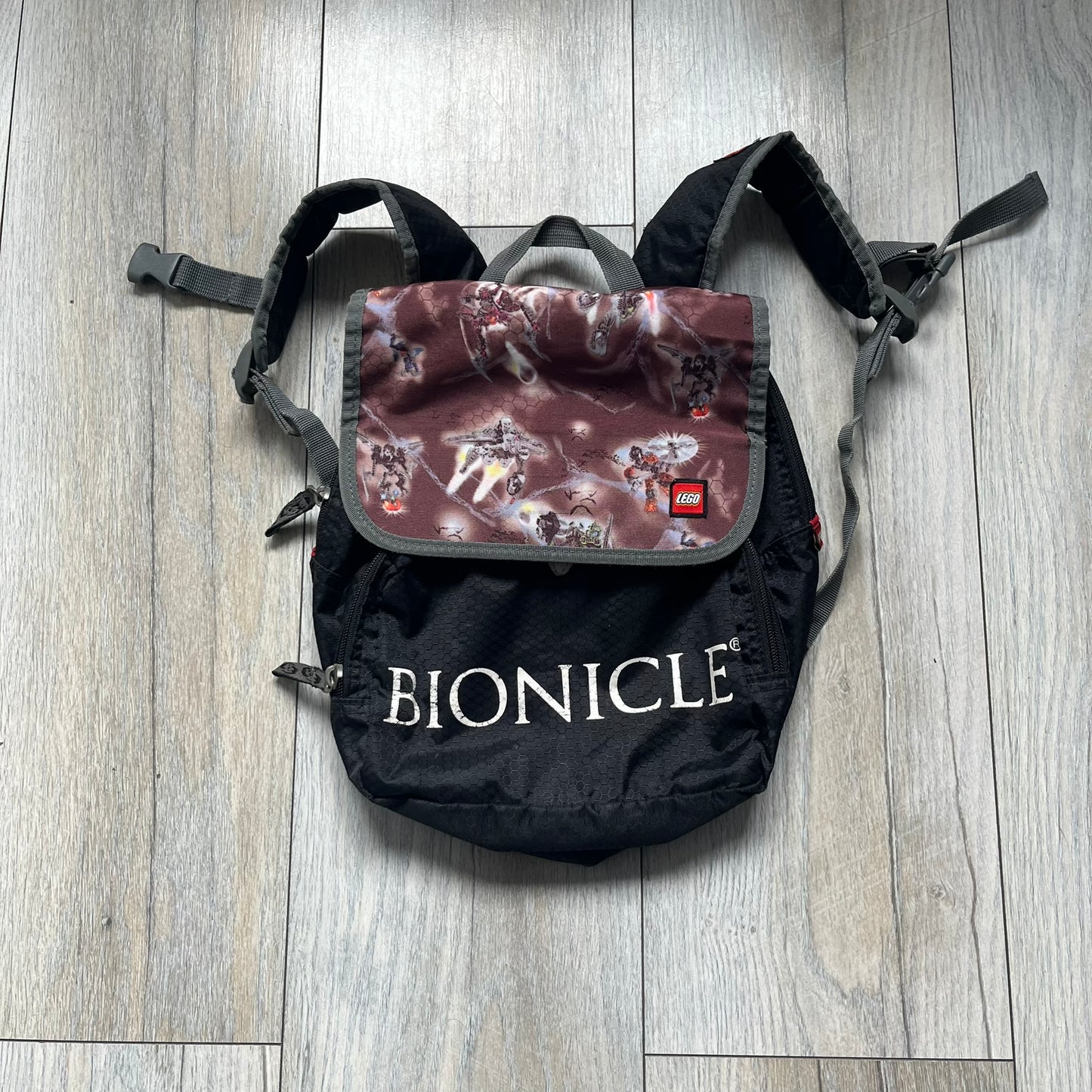 LEGO Bionicle 2009 Small Logo Backpack is a black backpack featuring a large white Bionicle logo on the lower front. The top flap section has a red all-over print with Bionicle characters and a LEGO logo patch. The interior includes a LEGO 2009 licensed tag.