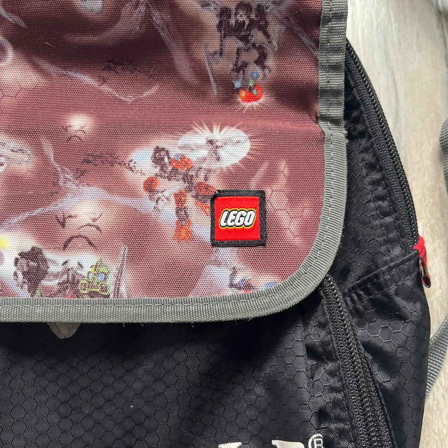 LEGO Bionicle 2009 Small Logo Backpack is a black backpack featuring a large white Bionicle logo on the lower front. The top flap section has a red all-over print with Bionicle characters and a LEGO logo patch. The interior includes a LEGO 2009 licensed tag.