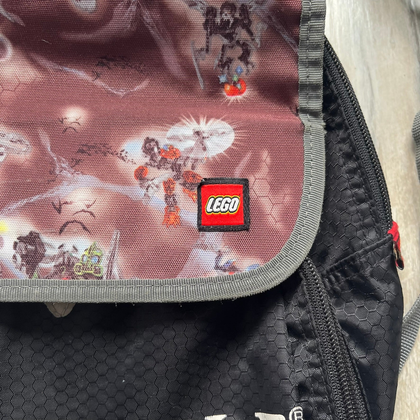 LEGO Bionicle 2009 Small Logo Backpack is a black backpack featuring a large white Bionicle logo on the lower front. The top flap section has a red all-over print with Bionicle characters and a LEGO logo patch. The interior includes a LEGO 2009 licensed tag.