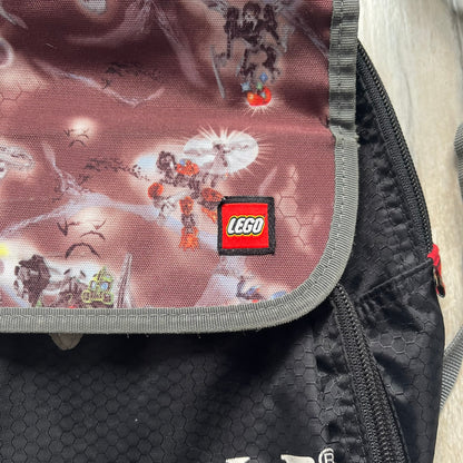 LEGO Bionicle 2009 Small Logo Backpack is a black backpack featuring a large white Bionicle logo on the lower front. The top flap section has a red all-over print with Bionicle characters and a LEGO logo patch. The interior includes a LEGO 2009 licensed tag.