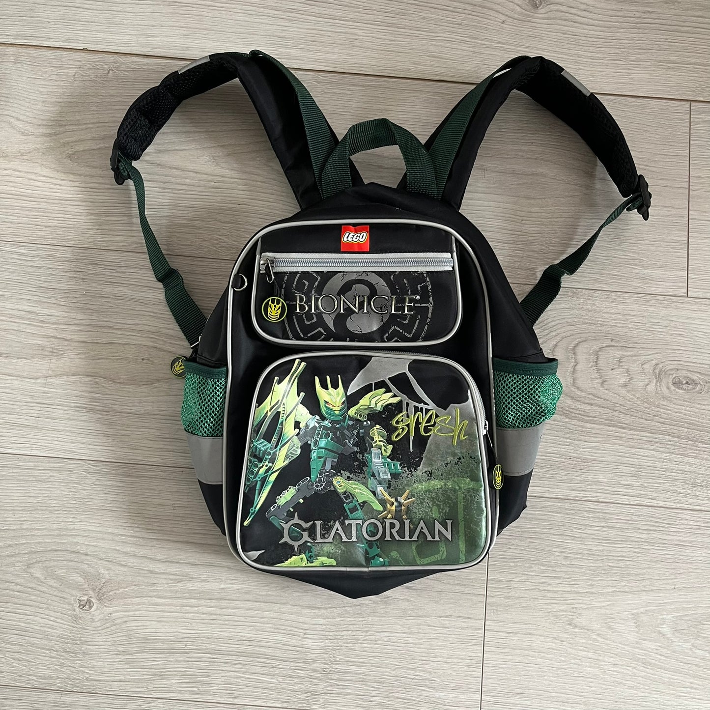 Lego Bionicle 2010 Glatorian Gresh Backpack made by Class Investment in 2010, featuring a front pocket with an embroidered Glatorian Gresh figure and text. The top pocket includes both Bionicle and LEGO logos, along with custom rubber zipper pulls. Finished with two side bottle pockets and additional Bionicle logo details, making it a great rare collectible for fans of the series.