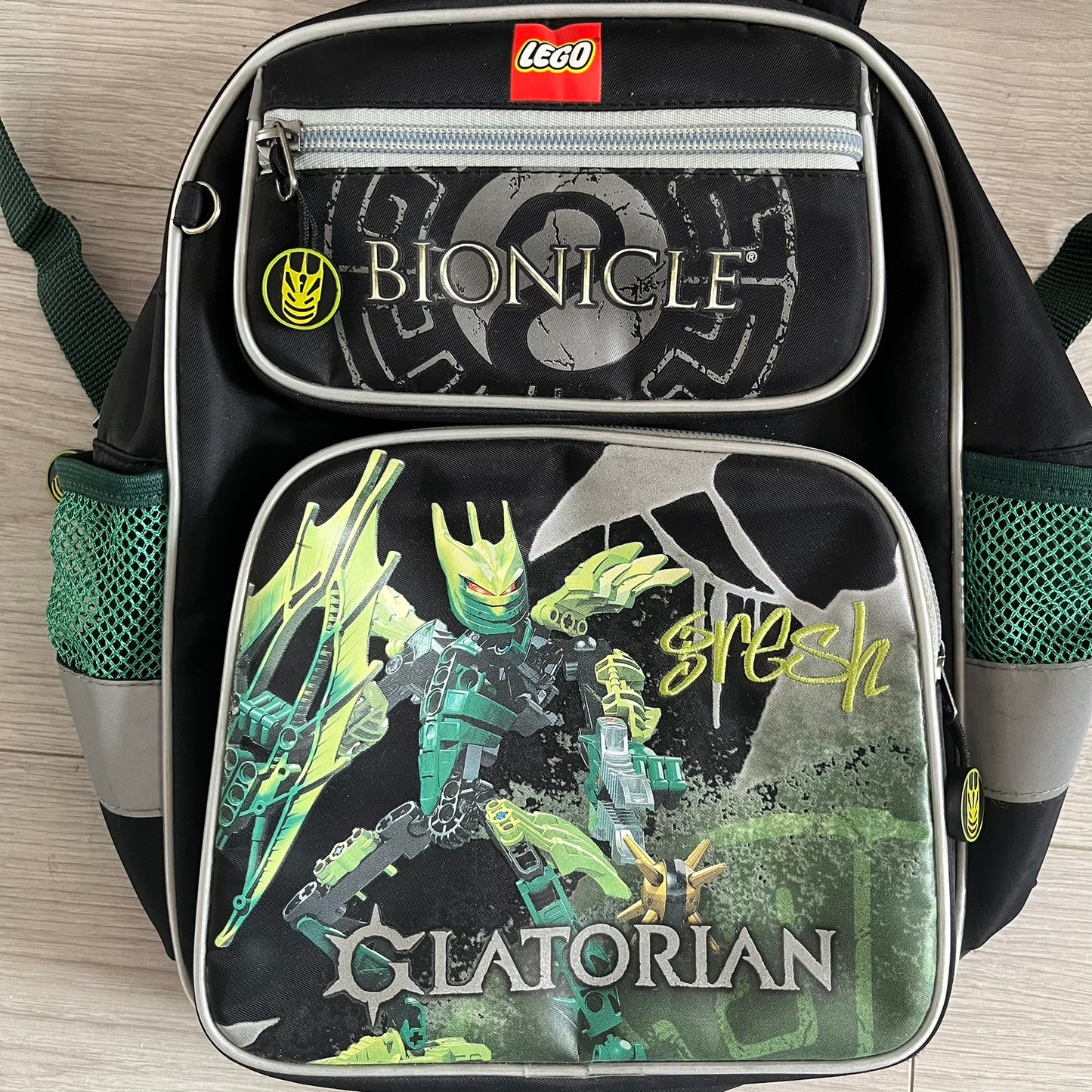 Lego Bionicle 2010 Glatorian Gresh Backpack made by Class Investment in 2010, featuring a front pocket with an embroidered Glatorian Gresh figure and text. The top pocket includes both Bionicle and LEGO logos, along with custom rubber zipper pulls. Finished with two side bottle pockets and additional Bionicle logo details, making it a great rare collectible for fans of the series.