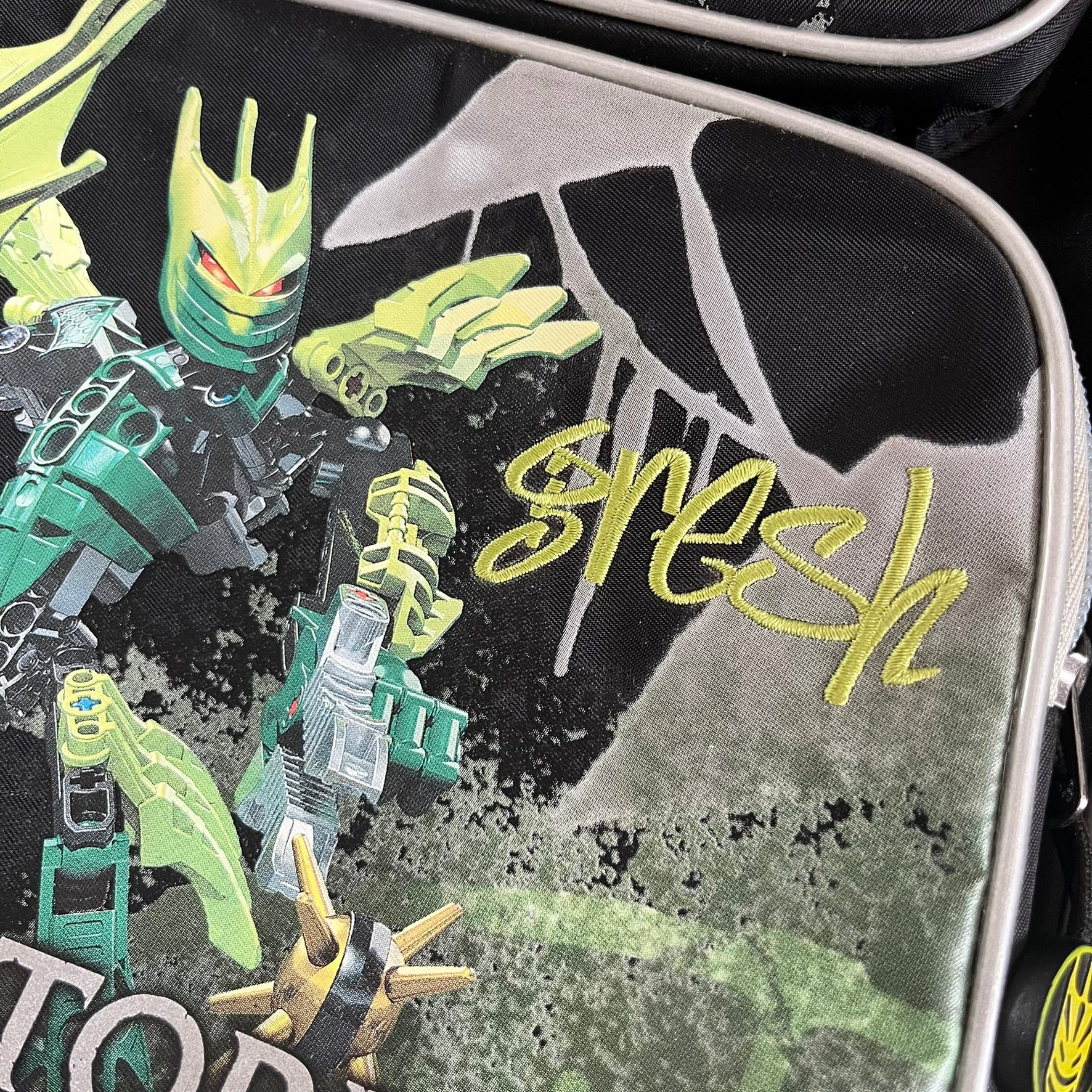 Lego Bionicle 2010 Glatorian Gresh Backpack made by Class Investment in 2010, featuring a front pocket with an embroidered Glatorian Gresh figure and text. The top pocket includes both Bionicle and LEGO logos, along with custom rubber zipper pulls. Finished with two side bottle pockets and additional Bionicle logo details, making it a great rare collectible for fans of the series.