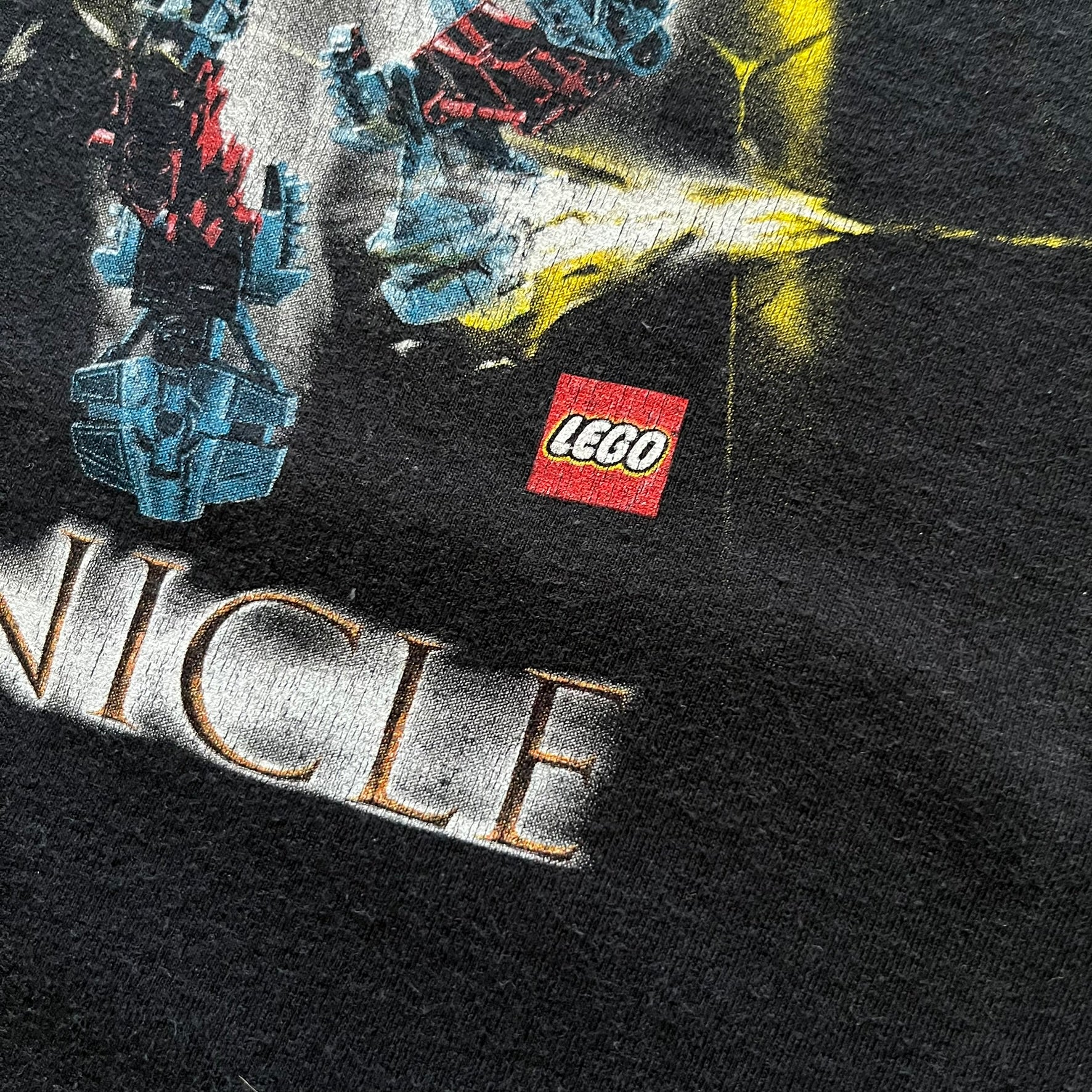 Rare 2000s Lego Bionicle T-shirt showcasing Toa Hordika Vakama from the 2005 set. Features the glowing Bionicle logo under the Binicle, small Lego branding and a naturally sunfaded black wash. A collectible tee that perfectly captures early-2000s nostalgia.