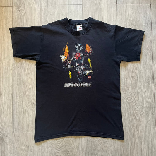Rare 2000s Lego Bionicle T-shirt showcasing Toa Hordika Vakama from the 2005 set. Features the glowing Bionicle logo under the Binicle, small Lego branding and a naturally sunfaded black wash. A collectible tee that perfectly captures early-2000s nostalgia.