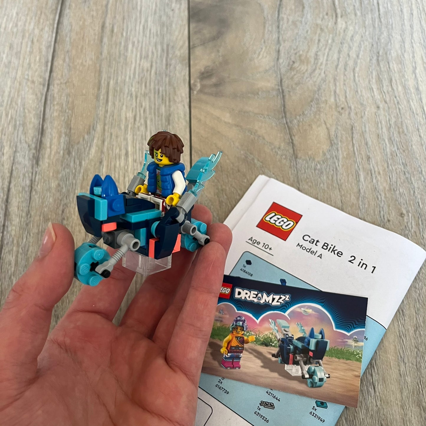 LEGO DREAMZzz Cat Bike 2-in-1 Make and Take Build is a limited promotional LEGO set distributed as an exclusive “make & take” event and not available for retail purchase. The model features a blue motorcycle with flame elements and a rider character wearing a blue vest. The build is designed as a 2-in-1 concept, allowing transformation into an alternate vehicle configuration.