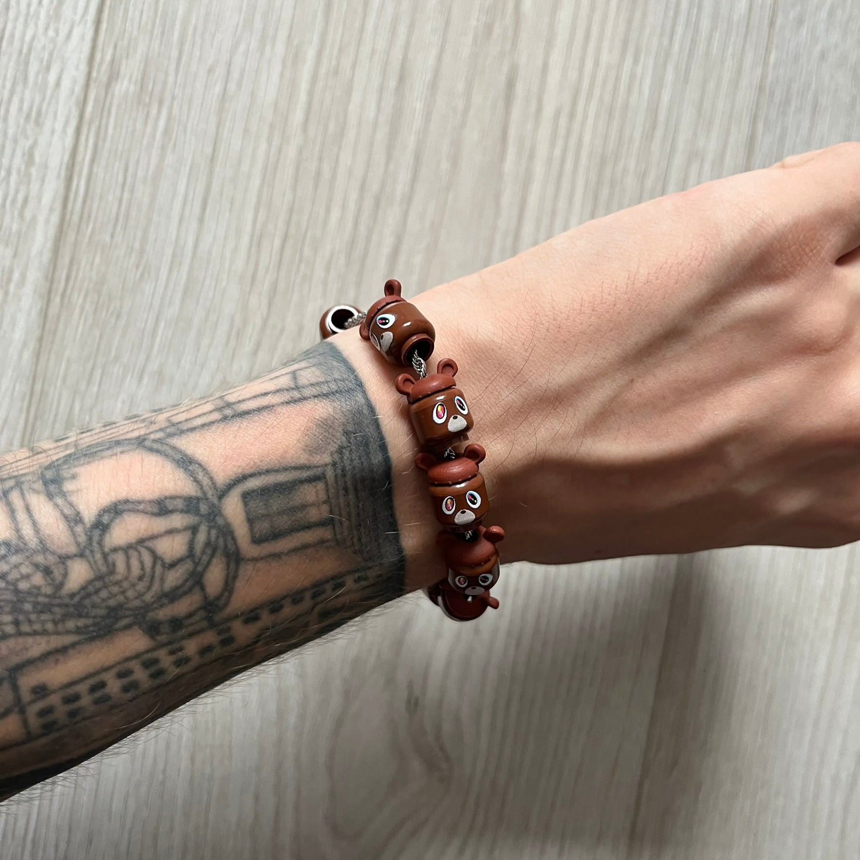 Lego Graduation Brick Bracelet featuring ten brown Lego bear heads from Kanye West’s Graduation era, set on a thin silver bracelet. The heads are standard Lego size and the piece comes in a custom-designed display box. Made by TheCanvasDon.