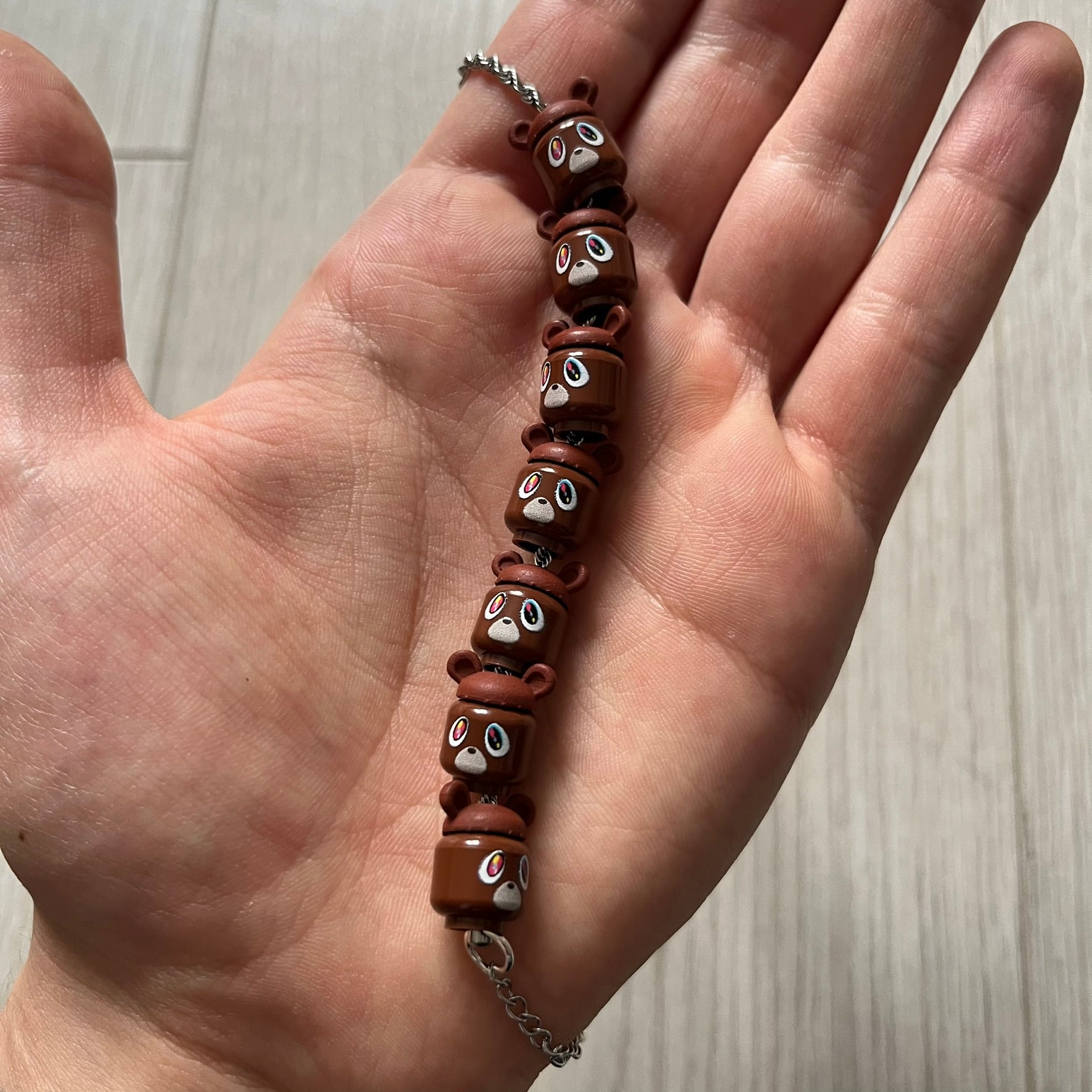 Lego Graduation Brick Bracelet featuring ten brown Lego bear heads from Kanye West’s Graduation era, set on a thin silver bracelet. The heads are standard Lego size and the piece comes in a custom-designed display box. Made by TheCanvasDon.