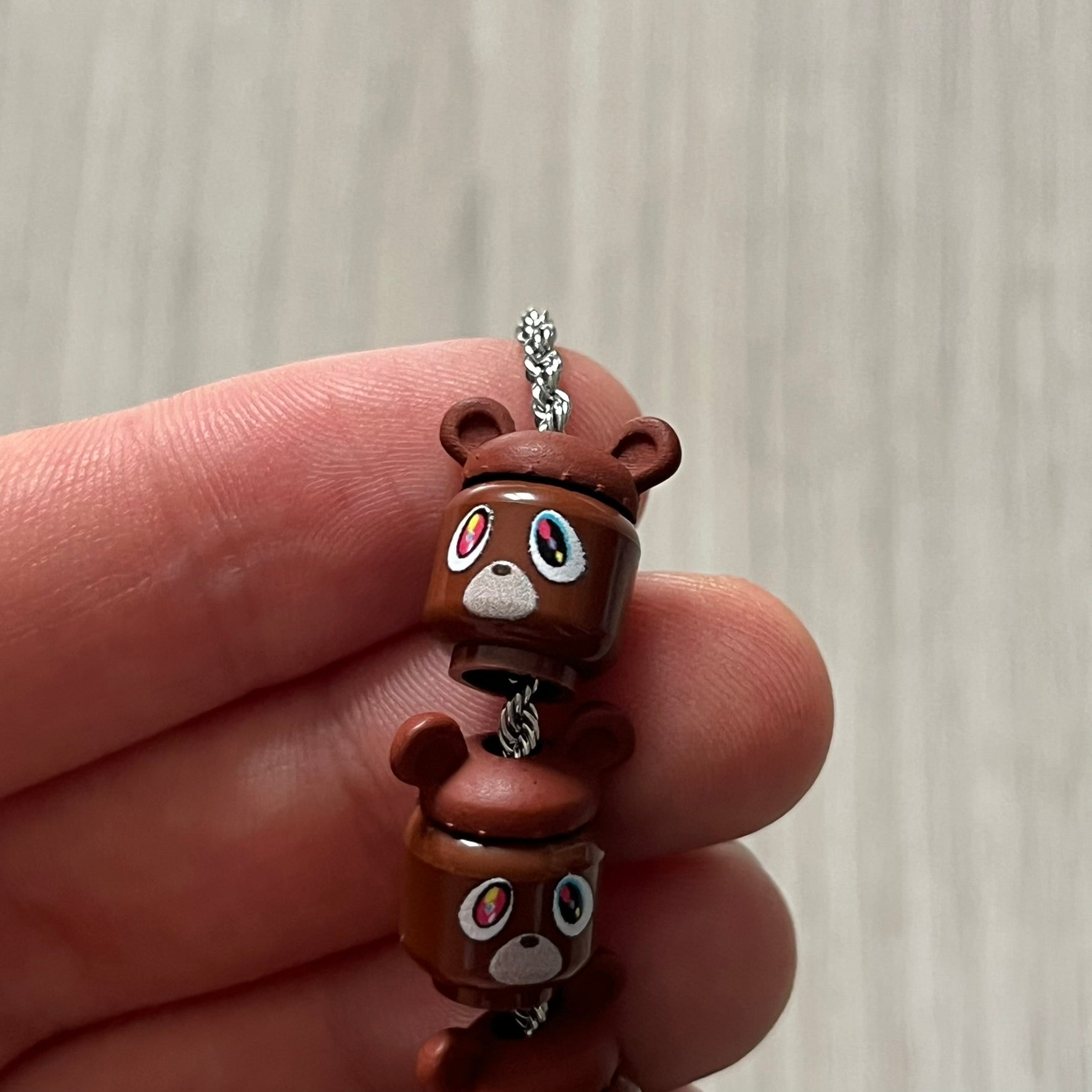Lego Graduation Brick Bracelet featuring ten brown Lego bear heads from Kanye West’s Graduation era, set on a thin silver bracelet. The heads are standard Lego size and the piece comes in a custom-designed display box. Made by TheCanvasDon.