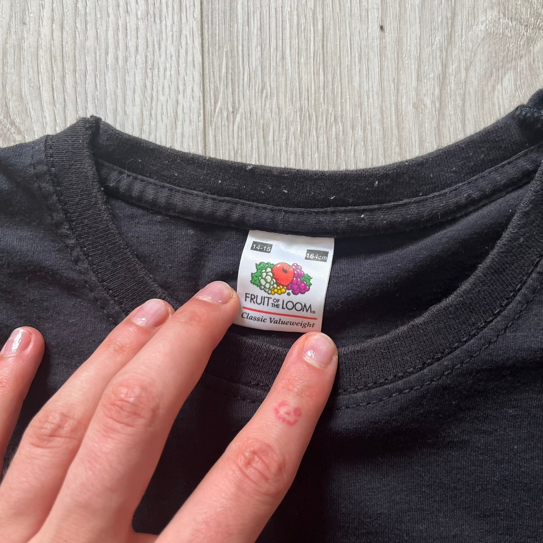 Hand holding a 'Fruit of the Loom' label on a black shirt against a wooden surface.