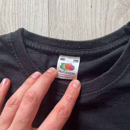 Hand holding a 'Fruit of the Loom' label on a black shirt against a wooden surface.