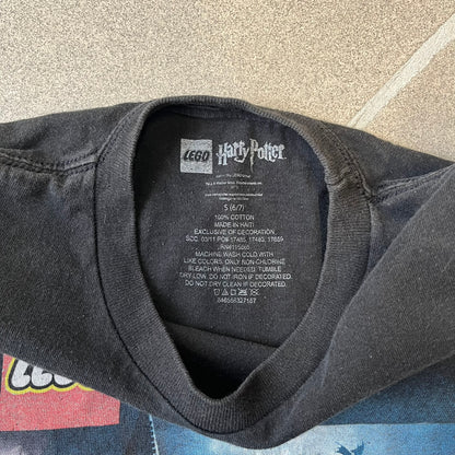 Lego Harry Potter: Years 1-4 Game 2011 Cover Tee is a black kids' T-shirt made from 100% cotton, featuring the game's cover artwork with classic characters and the Lego Harry Potter logo on the front. It carries a licensed 2011 Warner Bros. neck tag.