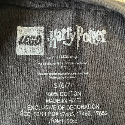 Lego Harry Potter: Years 1-4 Game 2011 Cover Tee is a black kids' T-shirt made from 100% cotton, featuring the game's cover artwork with classic characters and the Lego Harry Potter logo on the front. It carries a licensed 2011 Warner Bros. neck tag.