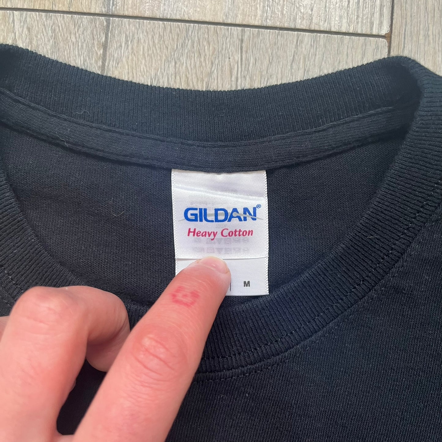 LEGO Minifigures “New Series” 2015 Tee is a black T-shirt featuring front and back prints. The front displays “LEGO Minifigures” text above eight characters arranged in a circle, with 2015 LEGO licensing and “New Series” text below. The back repeats the logo with a yellow minifigure in the center and “ASK ME” text underneath, likely produced as an employee promotional item.