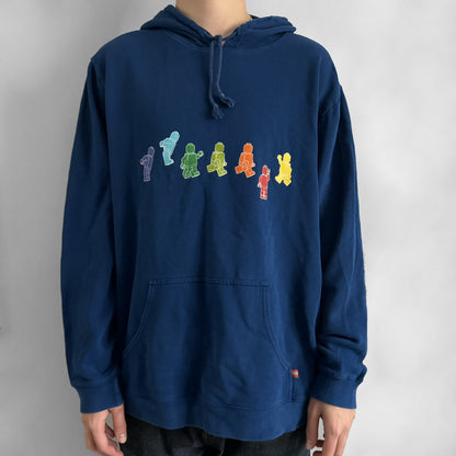 Lego Rainbow Minifigures Blue Hoodie from 2010, officially licensed by the Lego Group. Crafted from 100% cotton, it features seven colorful Lego minifigures in motion across the chest and a single red figure waving on the upper back. Designed in a bright blue colorway with a small Lego tag by the front pocket.