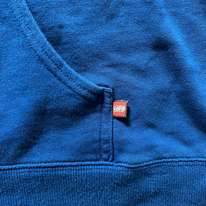 Lego Rainbow Minifigures Blue Hoodie from 2010, officially licensed by the Lego Group. Crafted from 100% cotton, it features seven colorful Lego minifigures in motion across the chest and a single red figure waving on the upper back. Designed in a bright blue colorway with a small Lego tag by the front pocket.