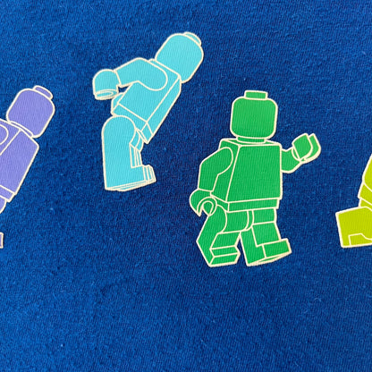 Lego Rainbow Minifigures Blue Tee from 2010, officially licensed by the Lego Group. Crafted from 100% cotton, it features seven colorful Lego minifigures in motion across the chest. Designed in a blue colorway with a small Lego tag on the left sleeve.