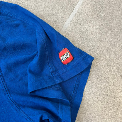 Lego Rainbow Minifigures Blue Tee from 2010, officially licensed by the Lego Group. Crafted from 100% cotton, it features seven colorful Lego minifigures in motion across the chest. Designed in a blue colorway with a small Lego tag on the left sleeve.