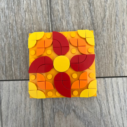 LEGO Rangoli Make and Take Build is a limited promotional LEGO set distributed as an exclusive “make & take” event and not available for retail purchase. The model features three small square rangoli-style builds arranged in decorative patterns. The designs use combinations of yellow, orange, red, brown, blue, and pink elements, with the first and third patterns matching each other.