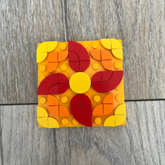 LEGO Rangoli Make and Take Build is a limited promotional LEGO set distributed as an exclusive “make & take” event and not available for retail purchase. The model features three small square rangoli-style builds arranged in decorative patterns. The designs use combinations of yellow, orange, red, brown, blue, and pink elements, with the first and third patterns matching each other.