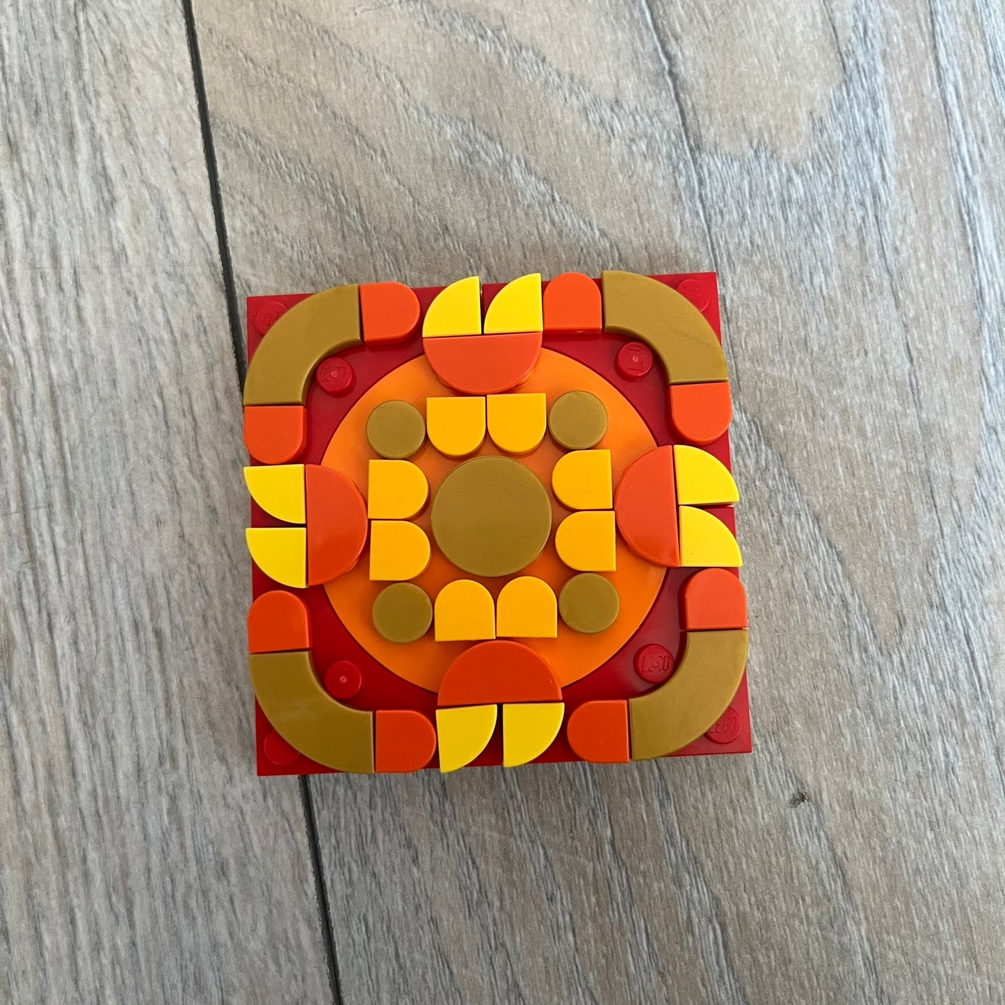 LEGO Rangoli Make and Take Build is a limited promotional LEGO set distributed as an exclusive “make & take” event and not available for retail purchase. The model features three small square rangoli-style builds arranged in decorative patterns. The designs use combinations of yellow, orange, red, brown, blue, and pink elements, with the first and third patterns matching each other.