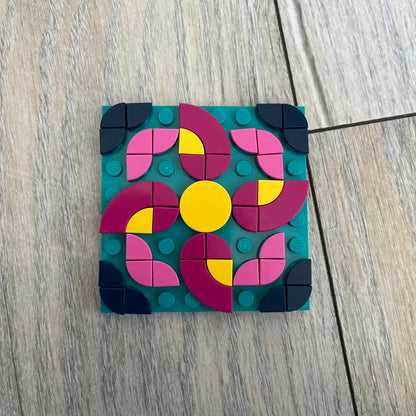 LEGO Rangoli Make and Take Build is a limited promotional LEGO set distributed as an exclusive “make & take” event and not available for retail purchase. The model features three small square rangoli-style builds arranged in decorative patterns. The designs use combinations of yellow, orange, red, brown, blue, and pink elements, with the first and third patterns matching each other.