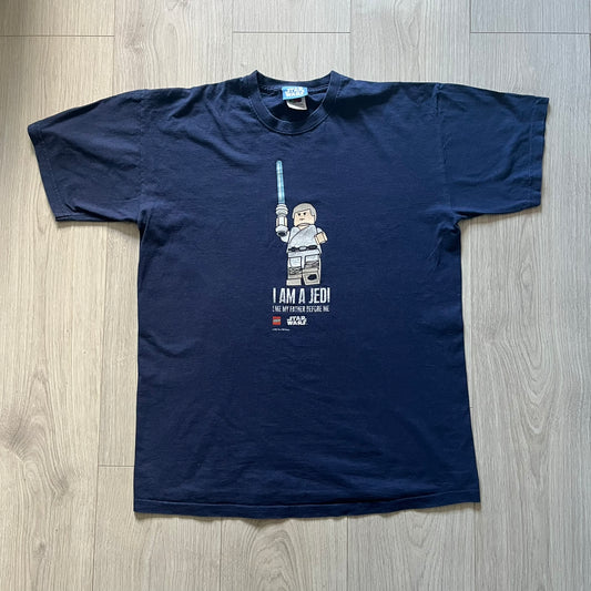 Vintage 2007 Lego Star Wars tee featuring Luke Skywalker with a lightsaber and the quote “I am a Jedi like my father before me.” Small Lego Star Wars logo sits underneath the graphic. Printed on a classic navy Fruit of the Loom blank perfect for collectors and SW fans.