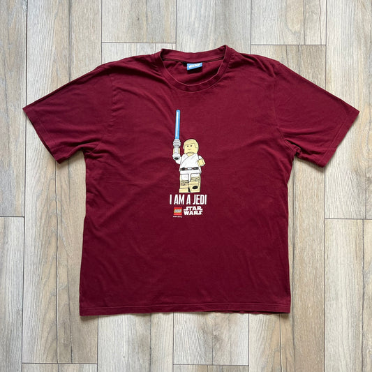 This Lego Star Wars 2008 Jedi Tee (Medium) in burgundy showcases Luke Skywalker wielding a blue lightsaber with a 'cracked' “I Am a Jedi” text. Officially licensed by Lego Star Wars, the tee includes authentic 2008 branding under the Luke minifigure graphic.